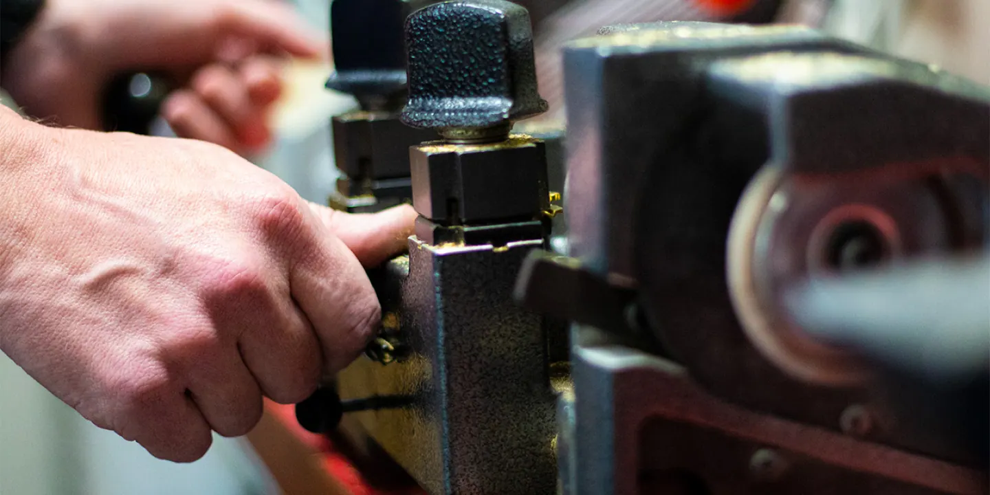 A locksmith's hands guiding a key blank through the duplicating machine